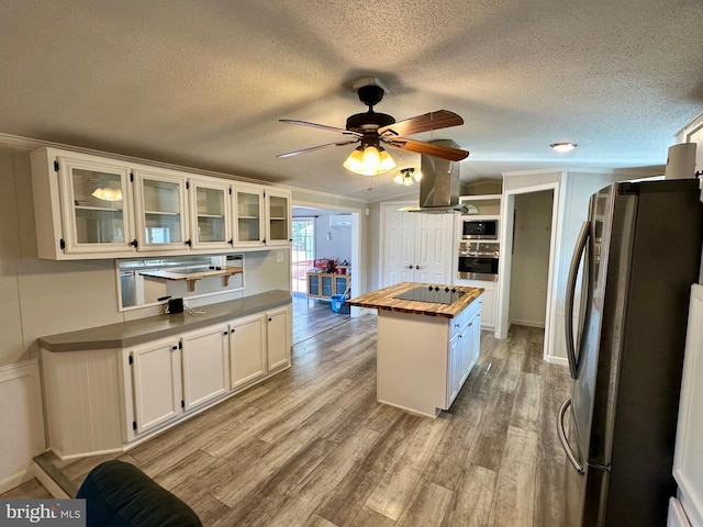 kitchen featuring white cabinets, wood counters, appliances with stainless steel finishes, a center island, and light wood-type flooring