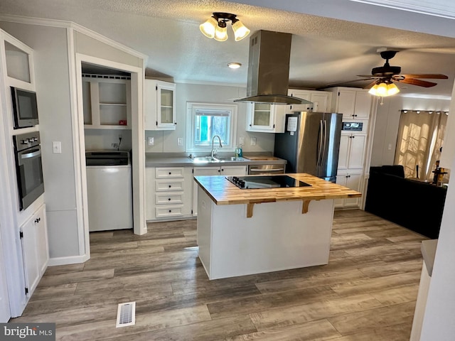 kitchen with butcher block counters, appliances with stainless steel finishes, washer / clothes dryer, island exhaust hood, and a sink