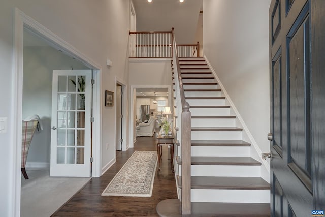 entryway featuring dark wood-type flooring, a towering ceiling, baseboards, and stairs