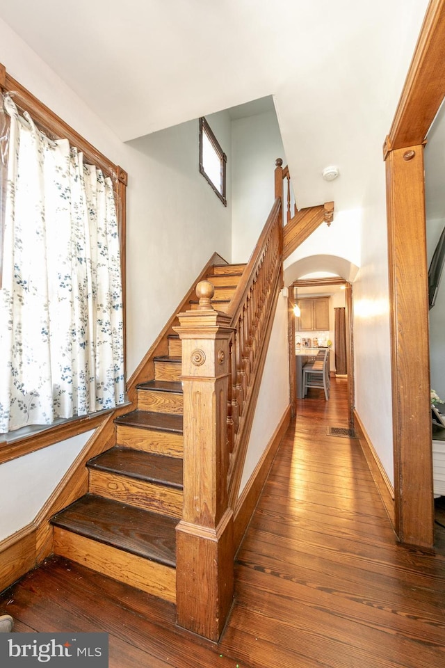 stairway featuring baseboards, arched walkways, and hardwood / wood-style floors