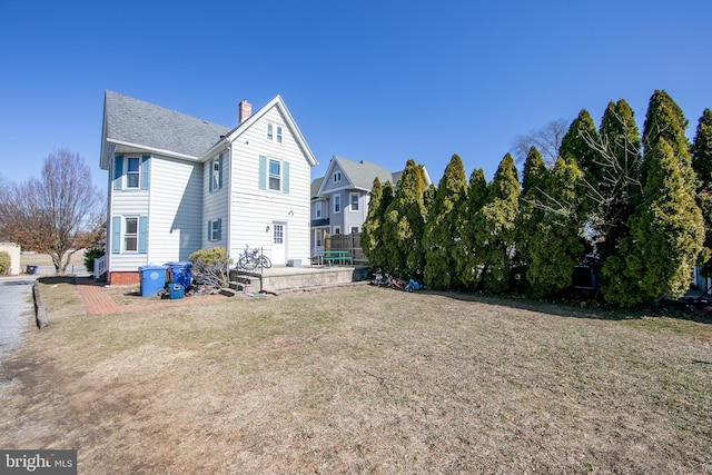 back of property featuring roof with shingles, a lawn, and a chimney