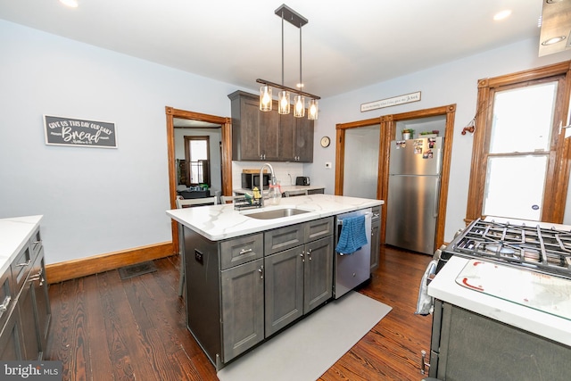 kitchen featuring appliances with stainless steel finishes, dark wood-style flooring, decorative light fixtures, a kitchen island with sink, and a sink