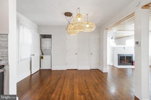 unfurnished dining area with wood finished floors, baseboards, a brick fireplace, plenty of natural light, and stacked washer and clothes dryer