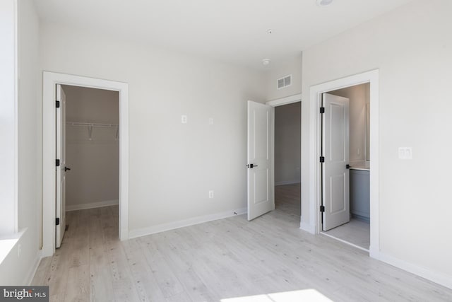 unfurnished bedroom with light wood-style flooring, a walk in closet, visible vents, and baseboards