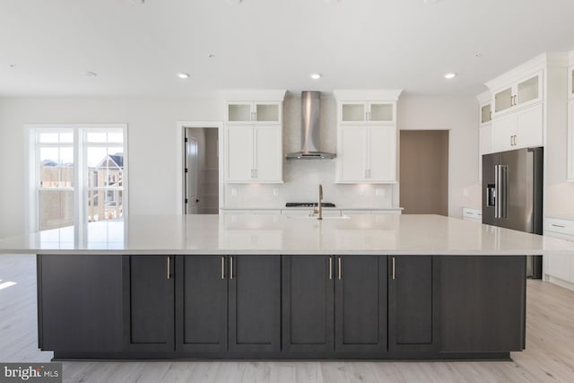 kitchen featuring a spacious island, high end refrigerator, white cabinetry, wall chimney range hood, and decorative backsplash