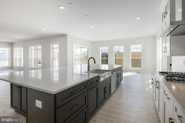 kitchen featuring stainless steel gas cooktop, a large island, white cabinetry, a sink, and wall chimney range hood