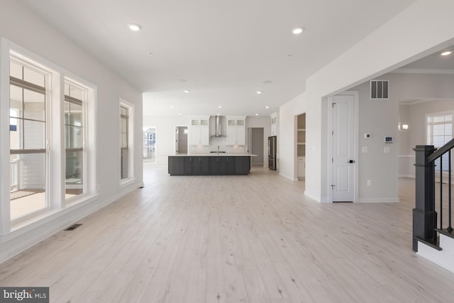 unfurnished living room featuring a wealth of natural light, stairway, visible vents, and light wood-style floors