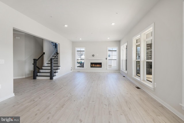 unfurnished living room featuring a lit fireplace, stairway, recessed lighting, and light wood-style floors