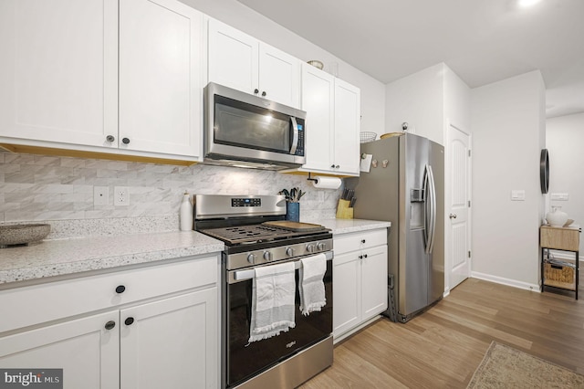 kitchen featuring light wood-style flooring, stainless steel appliances, white cabinetry, baseboards, and tasteful backsplash