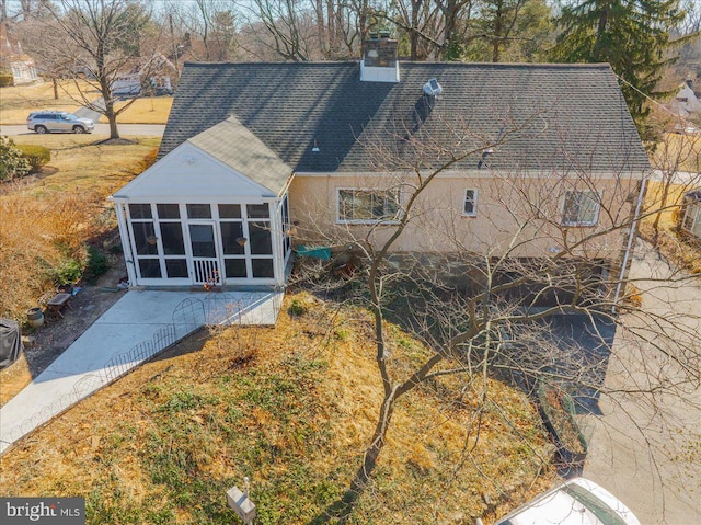 back of property featuring a shingled roof, a sunroom, a chimney, a patio area, and stucco siding