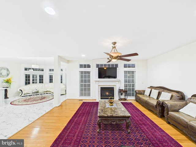 living room with a warm lit fireplace, baseboards, ceiling fan, wood finished floors, and recessed lighting