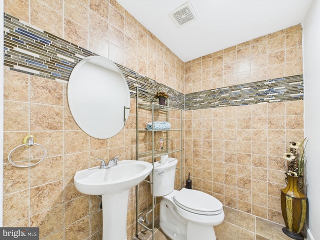 half bathroom with visible vents, a sink, tile walls, and toilet