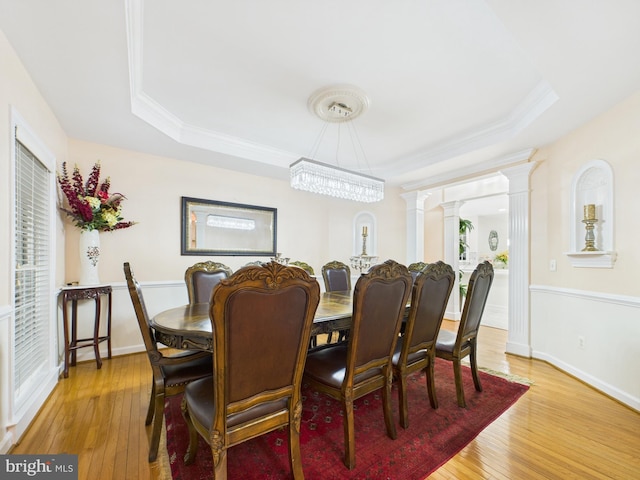 dining space with decorative columns, crown molding, a raised ceiling, and hardwood / wood-style floors