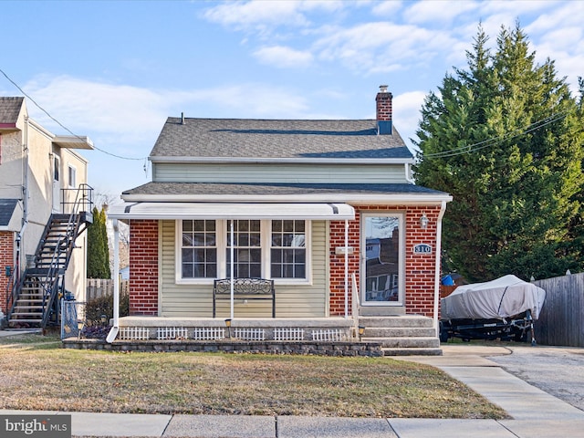 bungalow-style house featuring brick siding, fence, a chimney, and roof with shingles