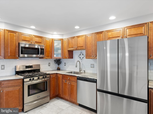 kitchen featuring brown cabinetry, stainless steel appliances, a sink, and light tile patterned flooring