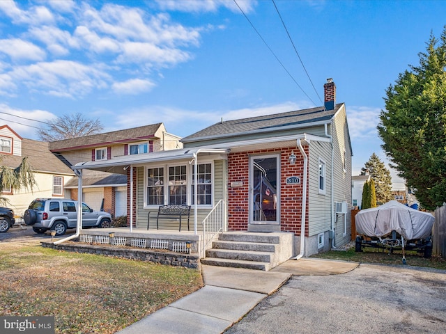 view of front of property featuring covered porch, brick siding, and a chimney