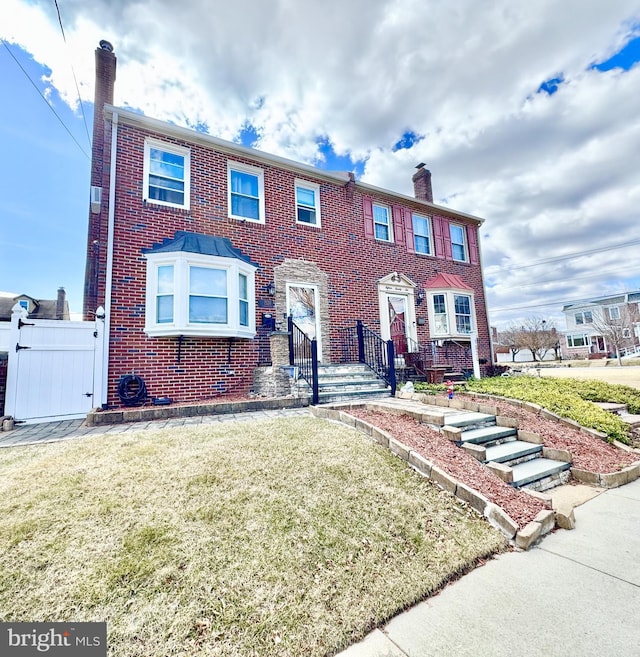 view of front facade featuring brick siding, a chimney, and a front yard