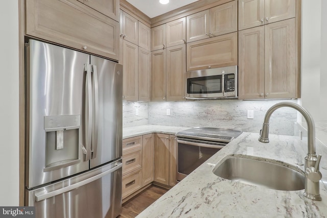 kitchen with decorative backsplash, light brown cabinetry, appliances with stainless steel finishes, a sink, and light stone countertops