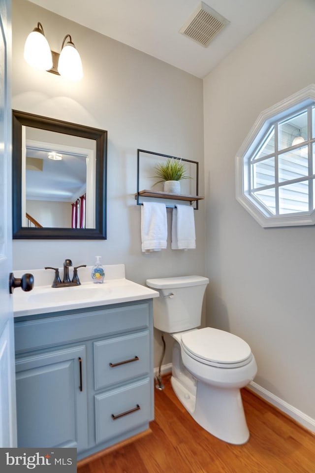 bathroom featuring visible vents, baseboards, toilet, wood finished floors, and vanity