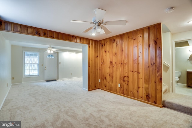 carpeted empty room with baseboards, wood walls, and a ceiling fan