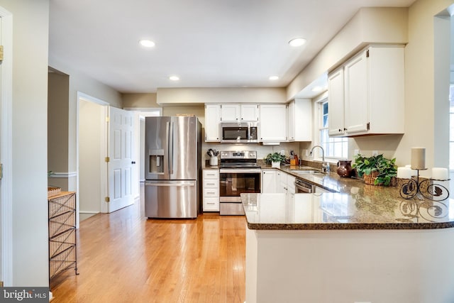 kitchen with a sink, stainless steel appliances, dark stone counters, a peninsula, and light wood finished floors