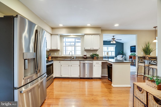 kitchen with a sink, a peninsula, white cabinetry, and stainless steel appliances