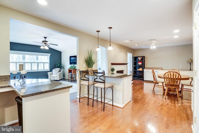 kitchen with light wood-type flooring, a peninsula, a fireplace, pendant lighting, and open floor plan