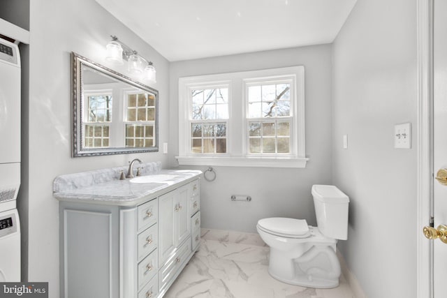 bathroom featuring toilet, stacked washer and dryer, vanity, baseboards, and marble finish floor