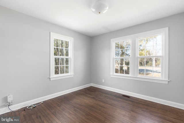 spare room featuring dark wood finished floors, visible vents, plenty of natural light, and baseboards