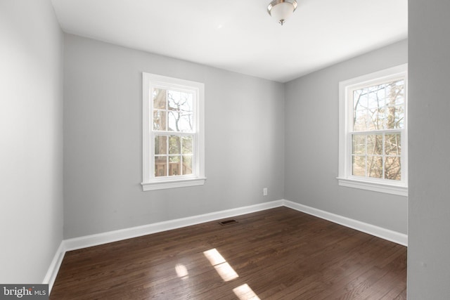 empty room with a healthy amount of sunlight, visible vents, baseboards, and dark wood-type flooring