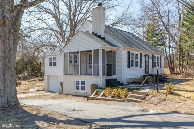 view of front of home with an attached garage, driveway, a chimney, and a shingled roof