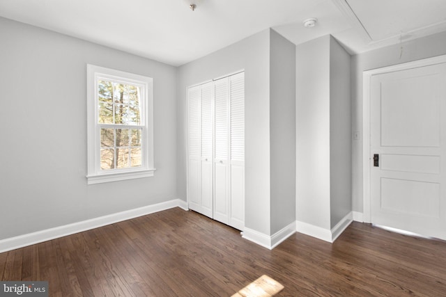 unfurnished bedroom with dark wood-style floors, attic access, baseboards, and a closet