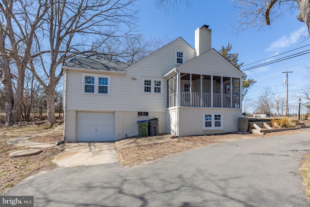 view of front of house featuring driveway, a chimney, an attached garage, and a sunroom