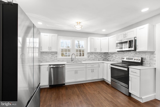 kitchen with appliances with stainless steel finishes, dark wood finished floors, a sink, and light countertops