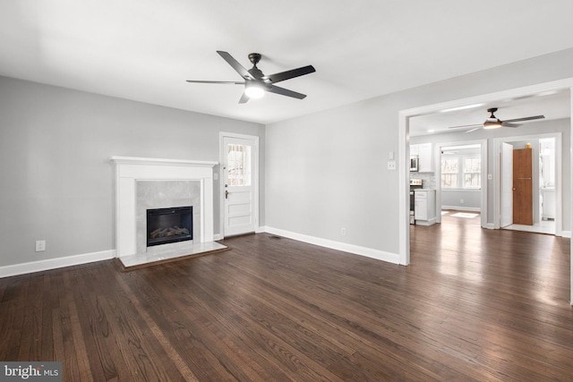 unfurnished living room featuring dark wood-style floors, a ceiling fan, baseboards, and a premium fireplace