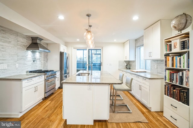 5664 Gainor Rd, Philadelphia, PA 19131 - kitchen with stainless steel appliances, a sink, an island with sink, light wood-type flooring, and wall chimney exhaust hood