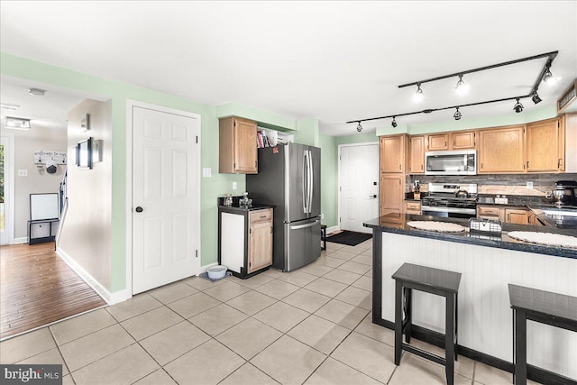 kitchen featuring dark countertops, backsplash, appliances with stainless steel finishes, a peninsula, and light tile patterned flooring