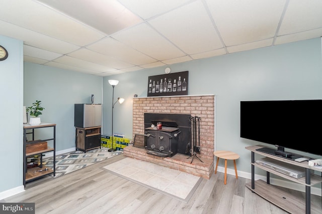 living room featuring baseboards, a paneled ceiling, wood finished floors, and a wood stove