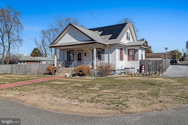 bungalow featuring fence, a porch, solar panels, and a front yard