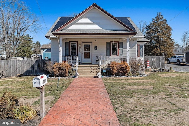 bungalow with a front yard, covered porch, roof with shingles, and fence