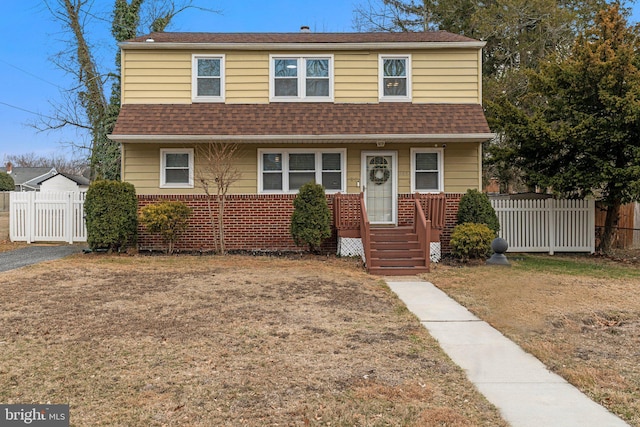 view of front of home featuring brick siding, roof with shingles, and fence