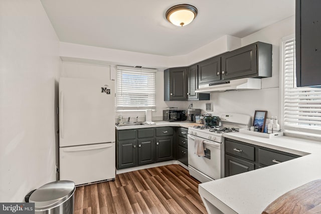 kitchen with dark wood-style flooring, light countertops, a sink, white appliances, and under cabinet range hood