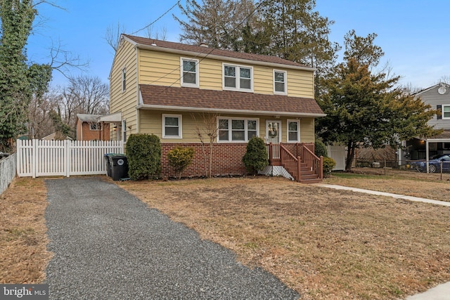 view of front of home featuring brick siding, a shingled roof, a front yard, fence, and driveway