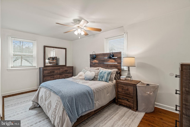 bedroom featuring a ceiling fan, multiple windows, baseboards, and wood finished floors