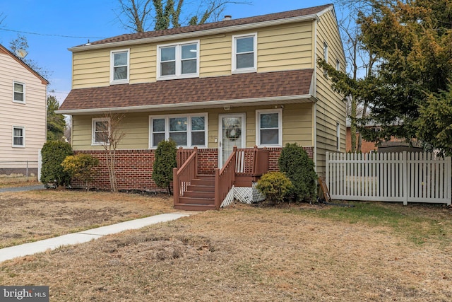 view of front facade featuring brick siding, roof with shingles, and fence