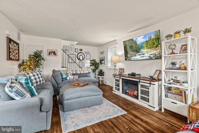 living area featuring stairs, wood finished floors, and a glass covered fireplace