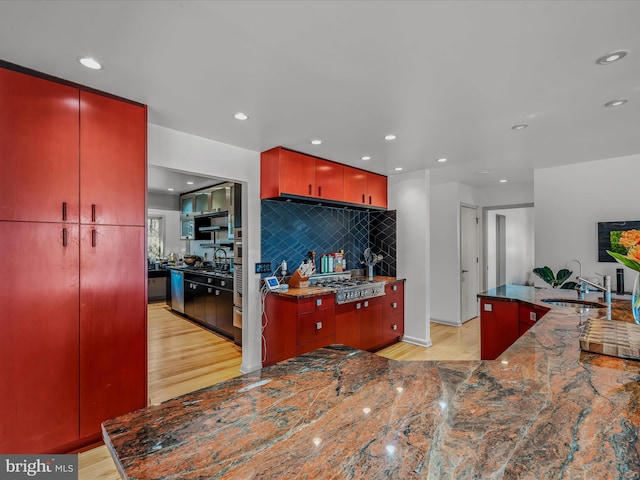 kitchen featuring a sink, appliances with stainless steel finishes, red cabinets, and light wood-style flooring