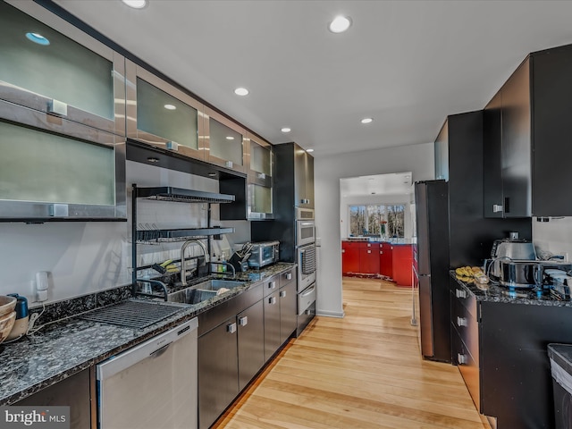 kitchen with stainless steel appliances, dark stone counters, a sink, and light wood finished floors