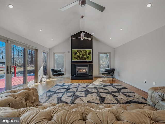 living room with vaulted ceiling, recessed lighting, a glass covered fireplace, and light wood-style floors