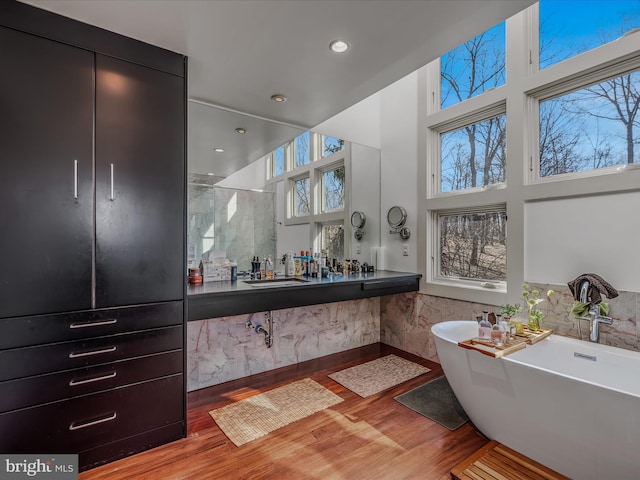 bathroom with a stall shower, a towering ceiling, wood finished floors, a freestanding tub, and recessed lighting